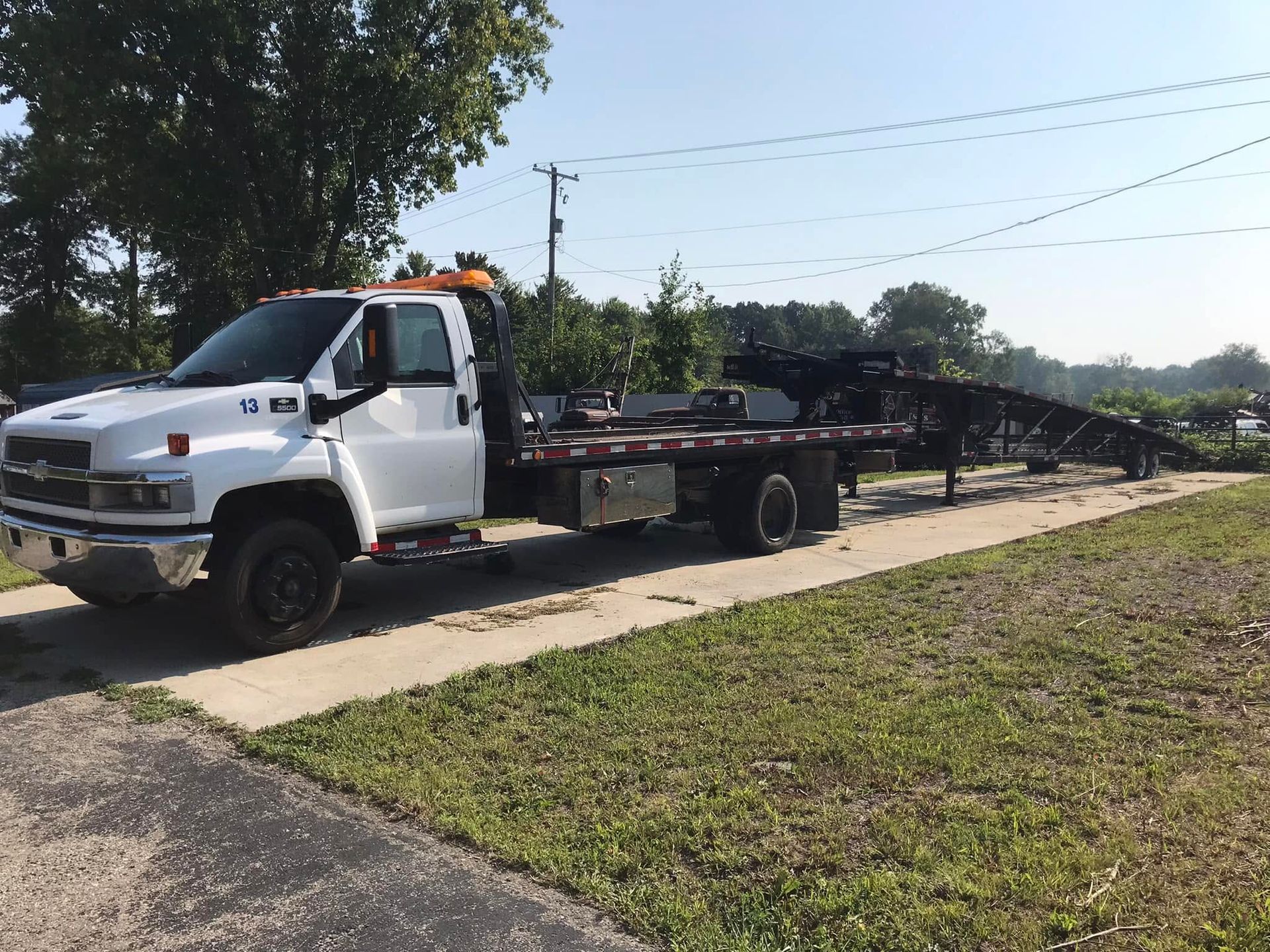 White flatbed tow truck parked on a roadside beside grass and trees