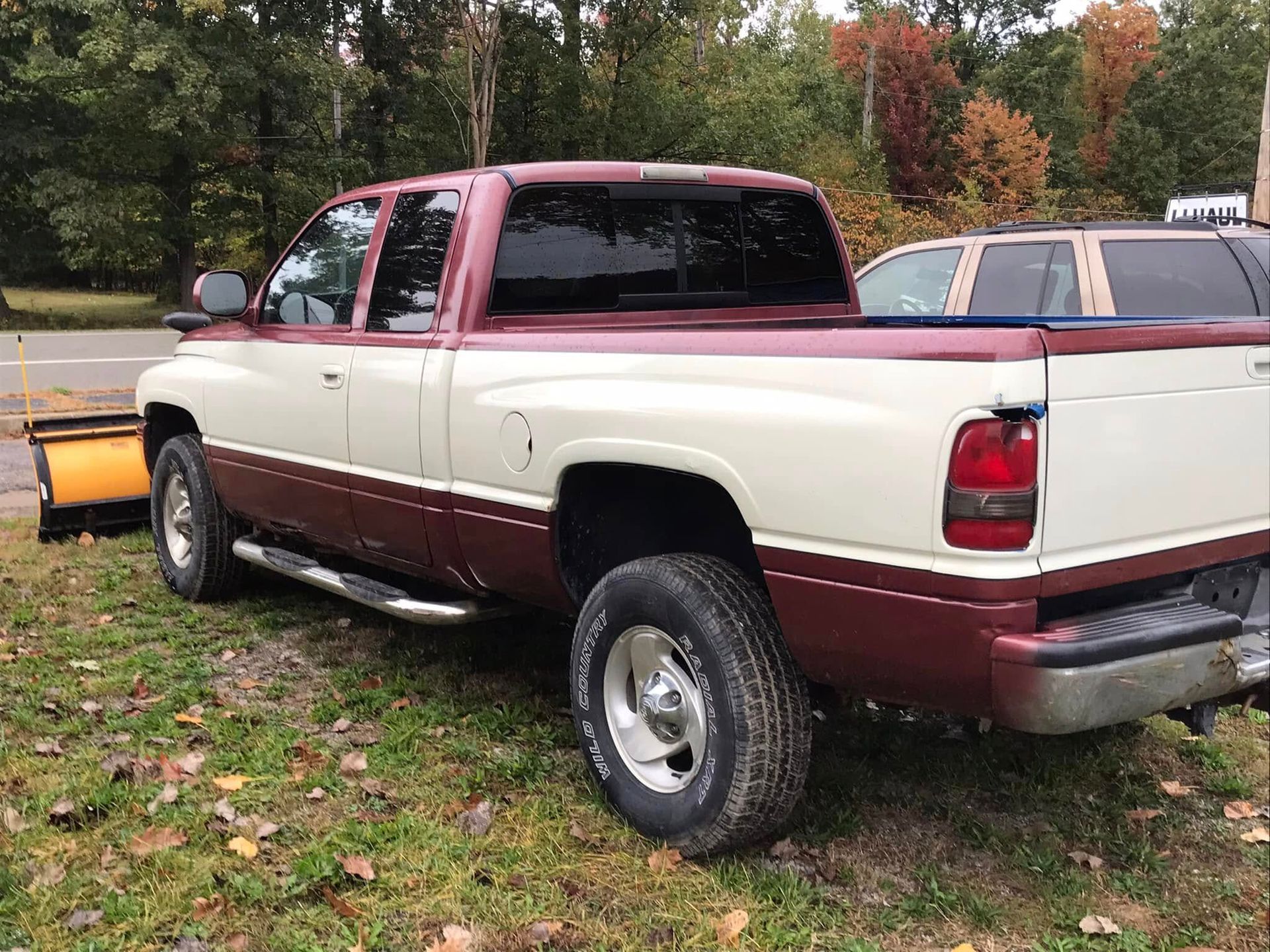 Two-tone red and white pickup truck parked on grass with autumn trees in the background