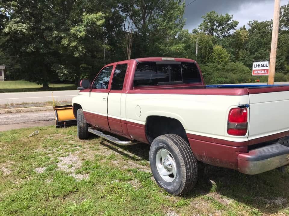 Two-tone red and white pickup truck parked on grass near a road and trees
