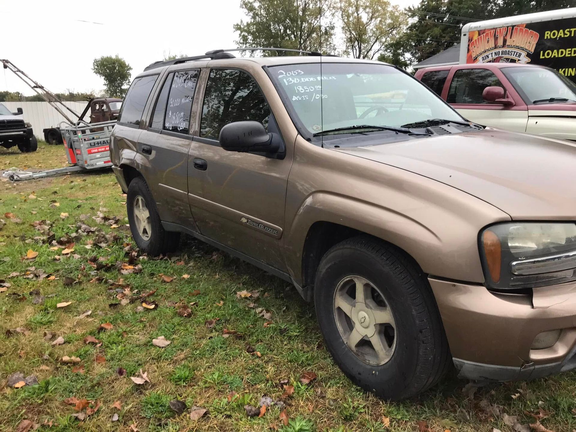 Brown SUV parked on grass at an outdoor lot, with other vehicles in the background.