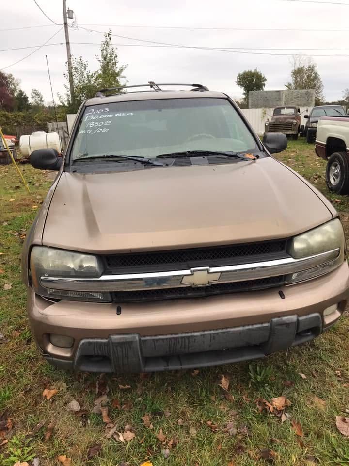 Beige Chevrolet SUV parked outdoors on a grassy lot with a damaged front grille and bumper.