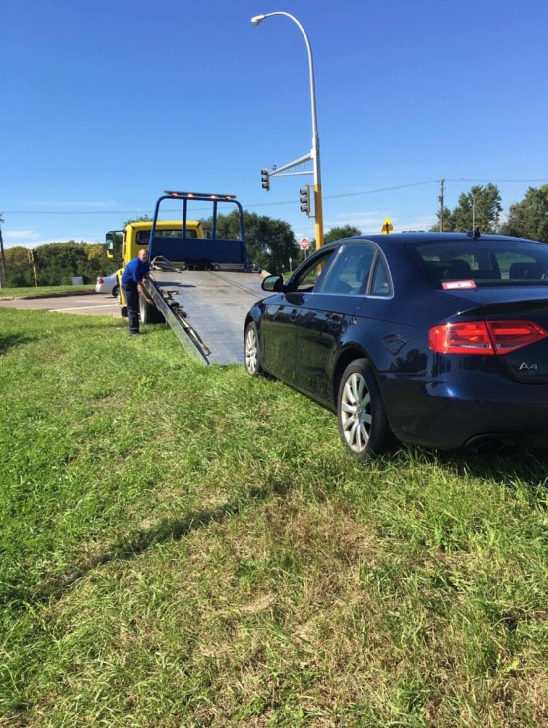Tow truck loading a dark blue sedan from a grassy roadside near an intersection