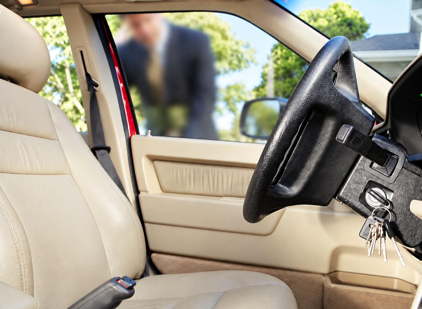 Beige car interior with steering wheel and front seat, open door, blurred figure outside.