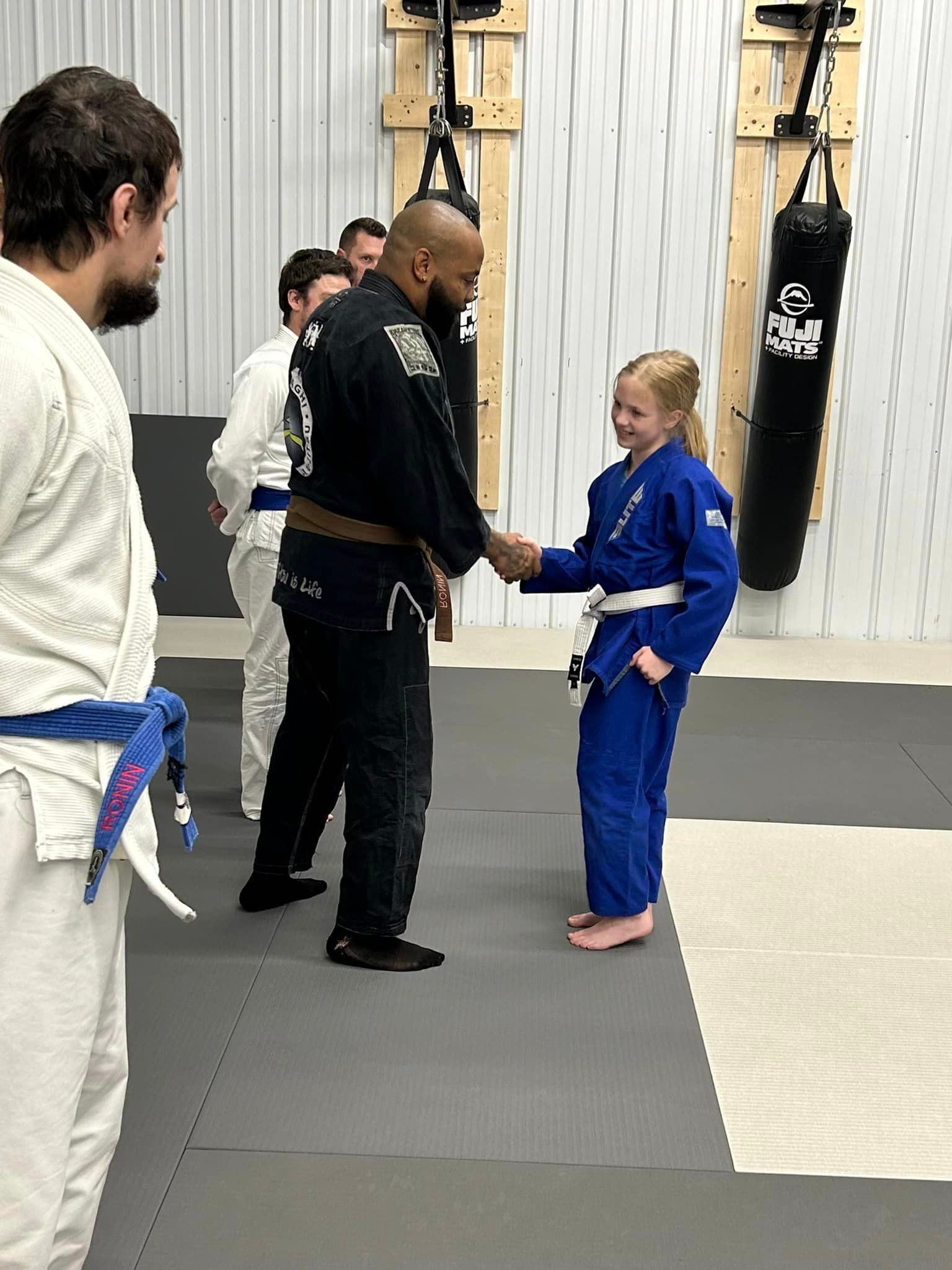 A man and a little girl are shaking hands in a gym.