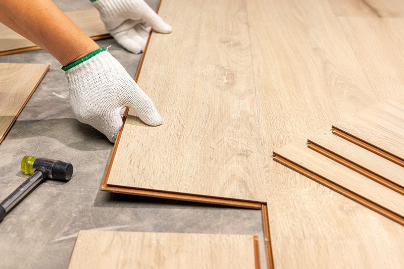 A person is installing a wooden floor with a hammer and gloves.