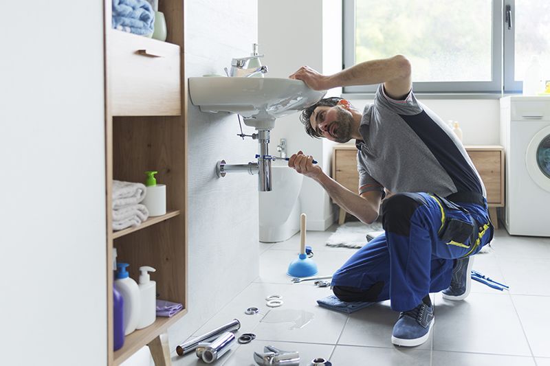 A plumber is fixing a sink in a bathroom.