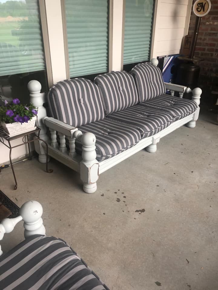 A light blue, wooden outdoor couch with grey striped cushions sits on a porch.