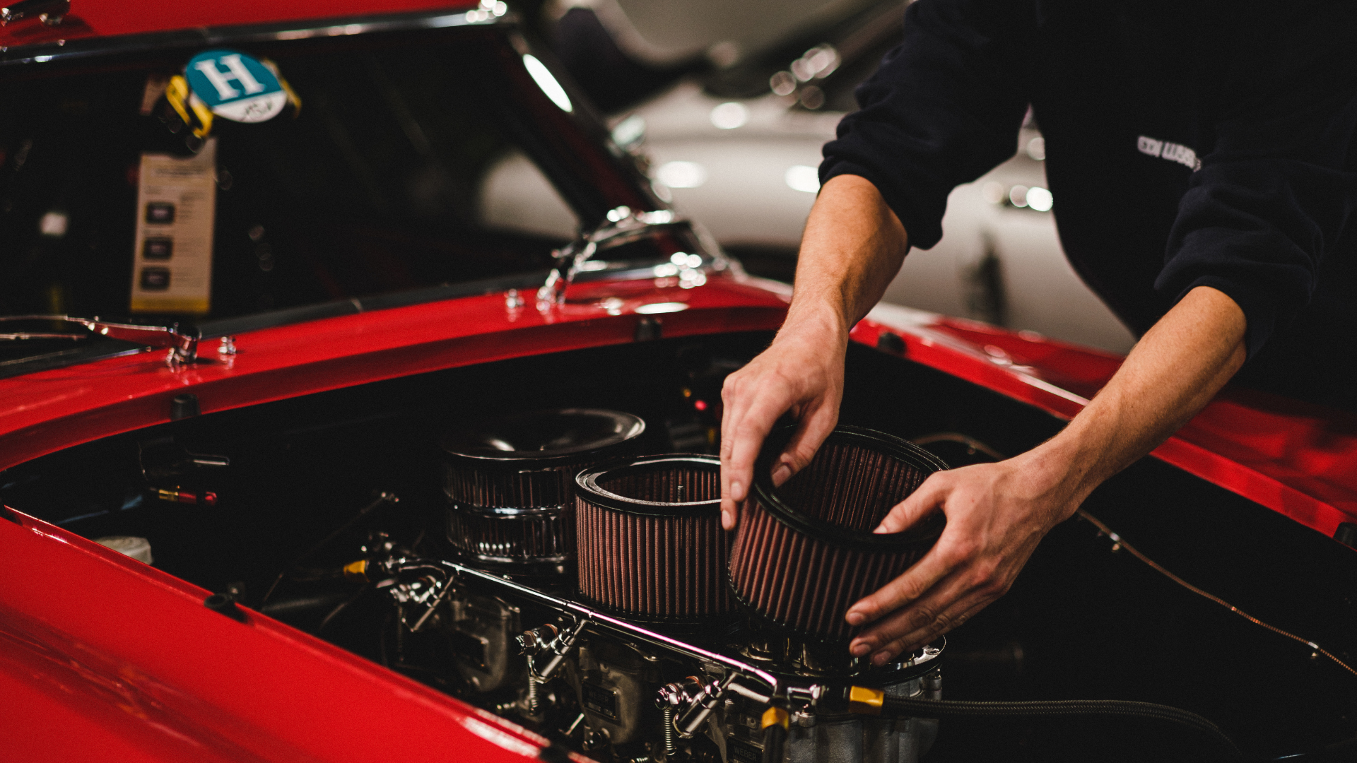 Mechanic installing an air filter in a red car engine bay at a car show