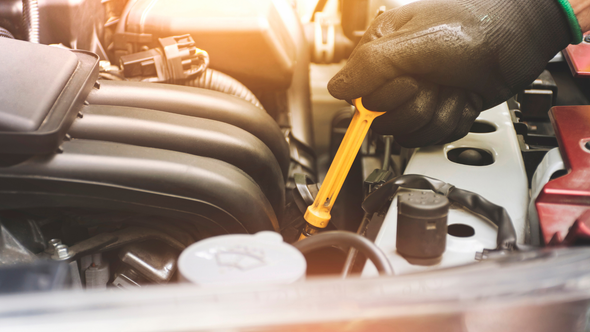 Gloved hand checking engine oil with a dipstick in a car engine bay