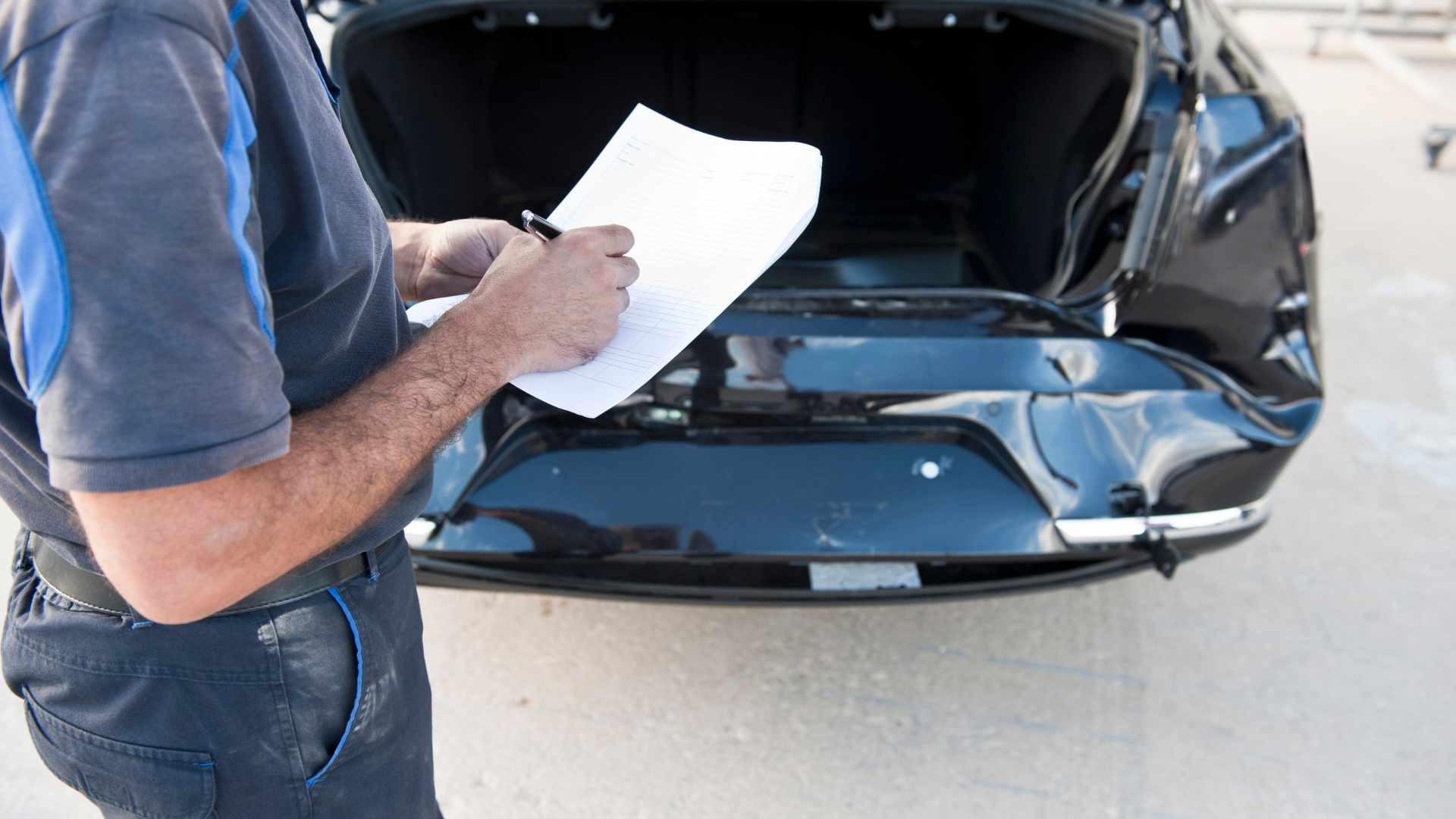 Person writing on a clipboard beside an open black car hood