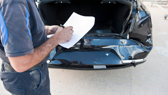 Person writing on a clipboard beside an open black car hood