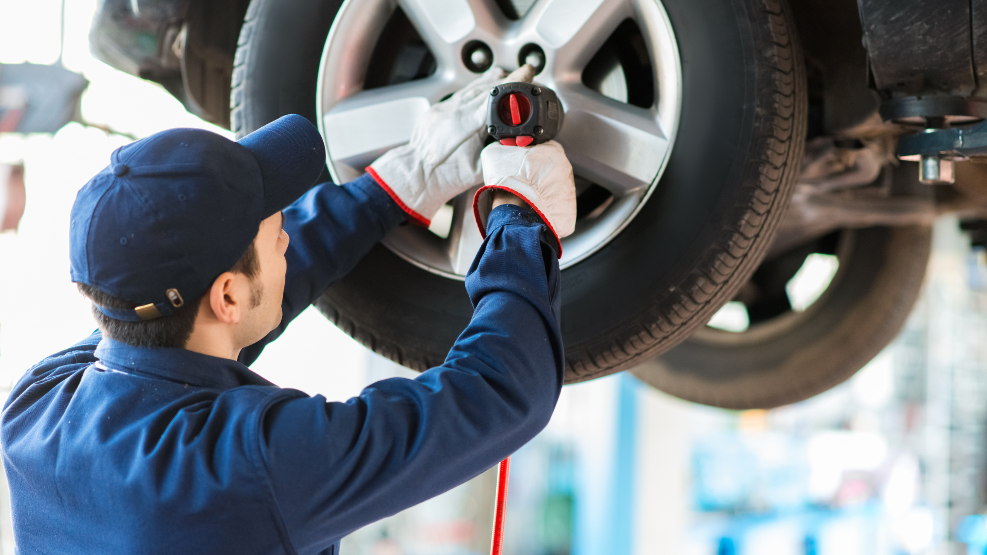 Mechanic in blue uniform using a torque wrench to tighten a car wheel on a lifted vehicle