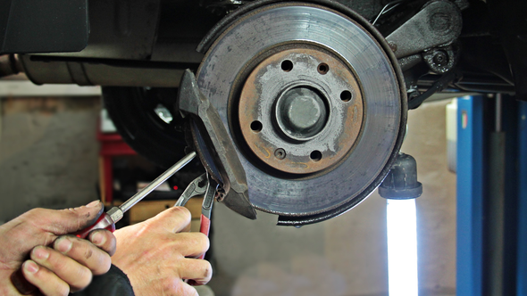 Mechanic using tools to work on a car’s exposed brake rotor in a garage
