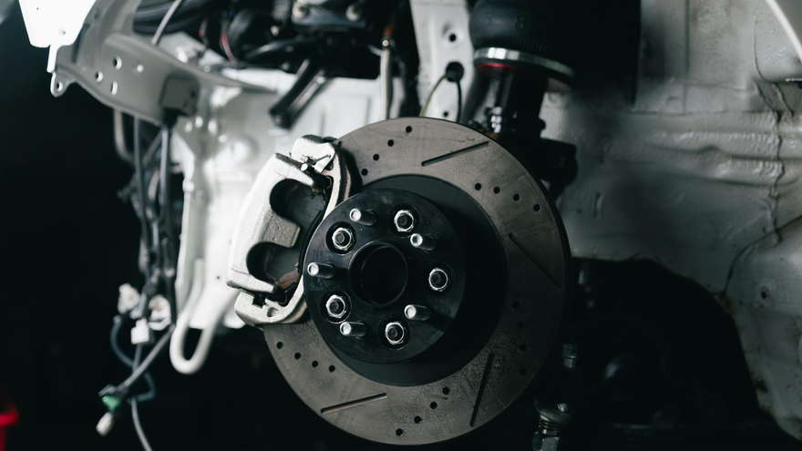 Close-up of a car brake rotor and caliper inside a wheel well, with metal components visible.