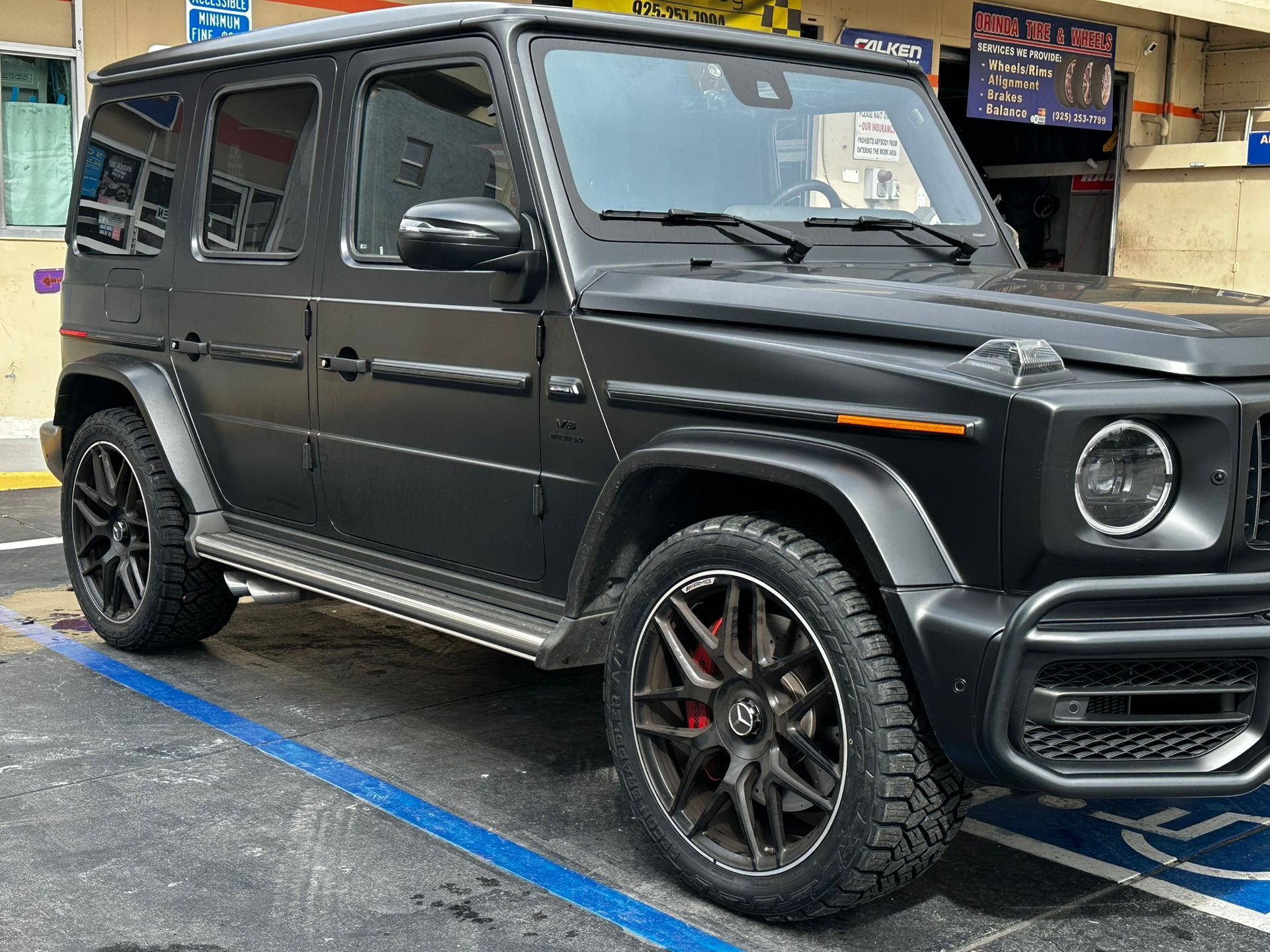 A matte black Mercedes-Benz G-Class SUV parked in a parking space with red brake calipers visible on the wheels.