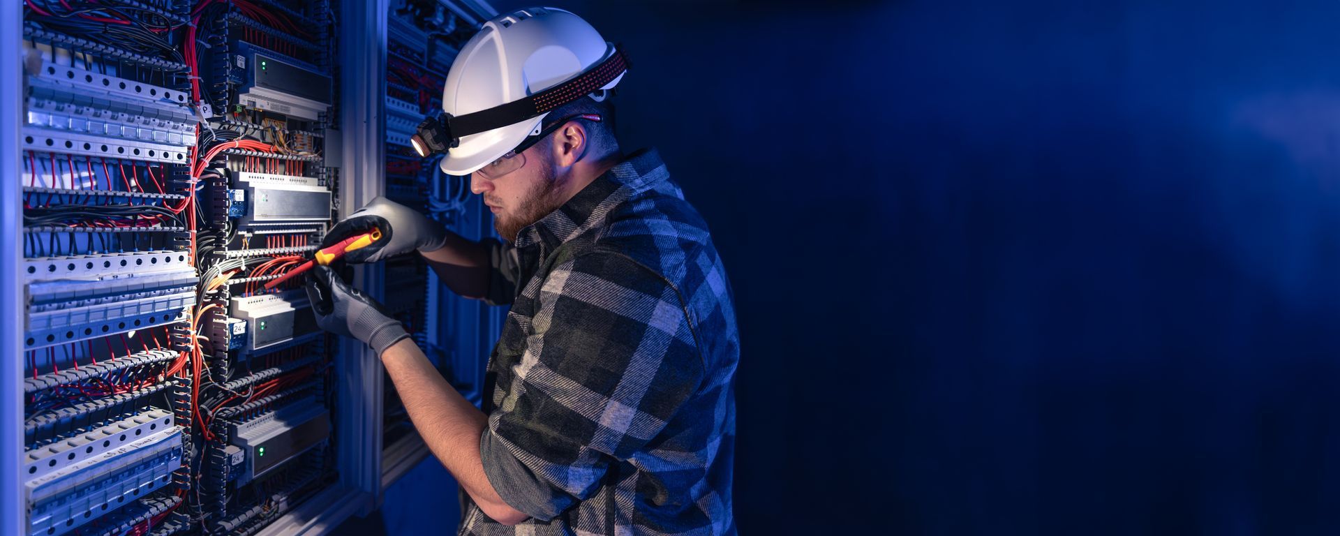 Electrician inspecting and testing wiring inside an industrial electrical control panel.