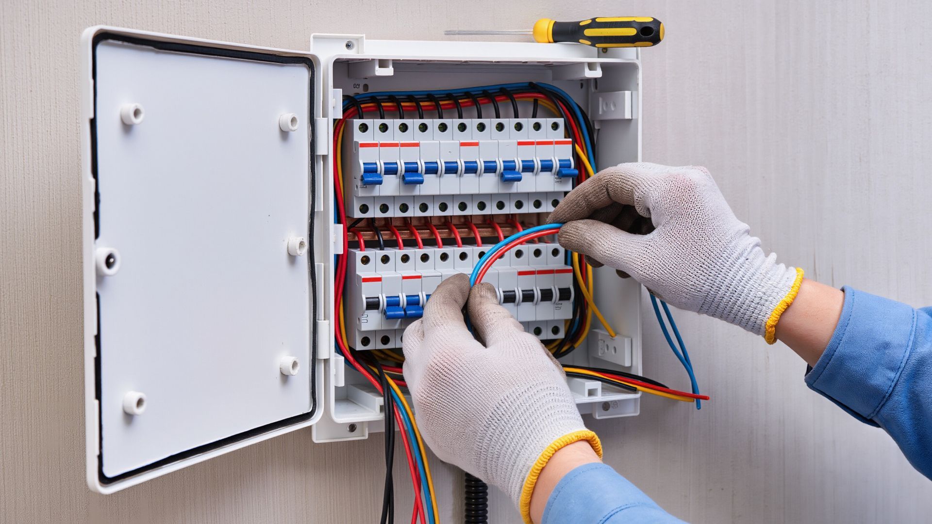Gloved hands adjusting circuit breakers in open panel with colorful wiring for electrical work