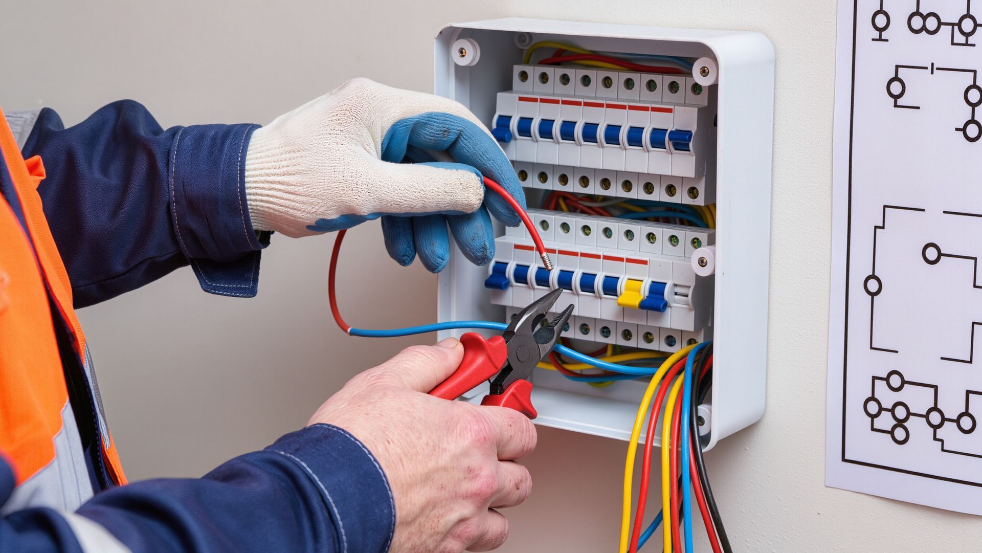 An electrician holds a digital multimeter, examining colorful wires inside a circuit breaker panel.