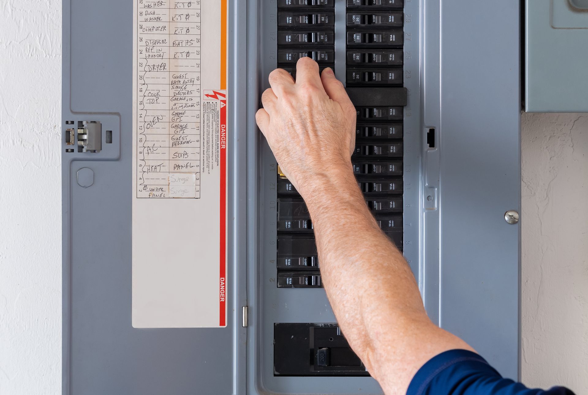 Person's hand flipping a circuit breaker switch in a gray electrical panel.