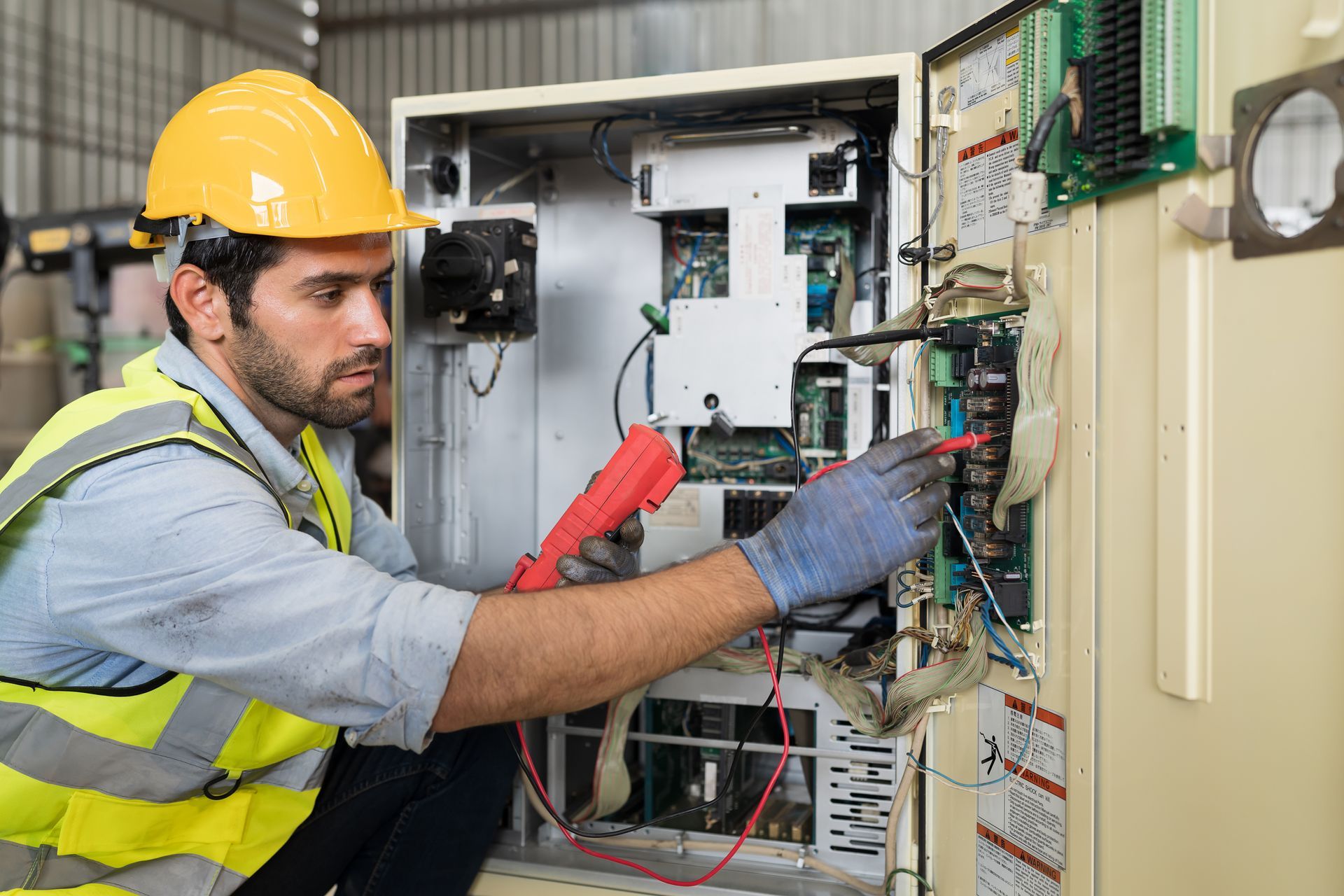 An electrician wearing a hard hat and safety vest is checking the operation of an electric system.