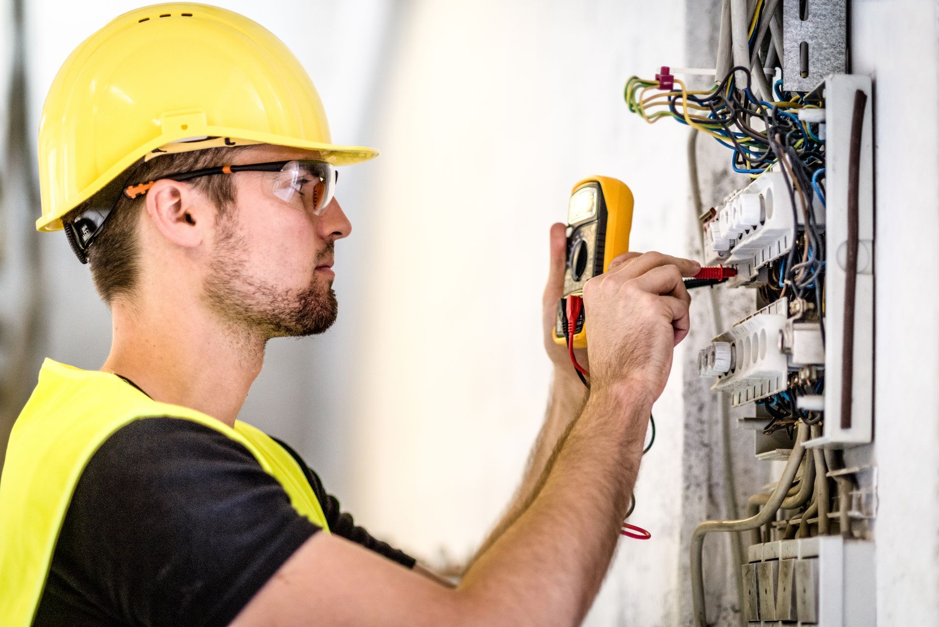 An electrician using a multimeter to check electrical wiring in a panel.