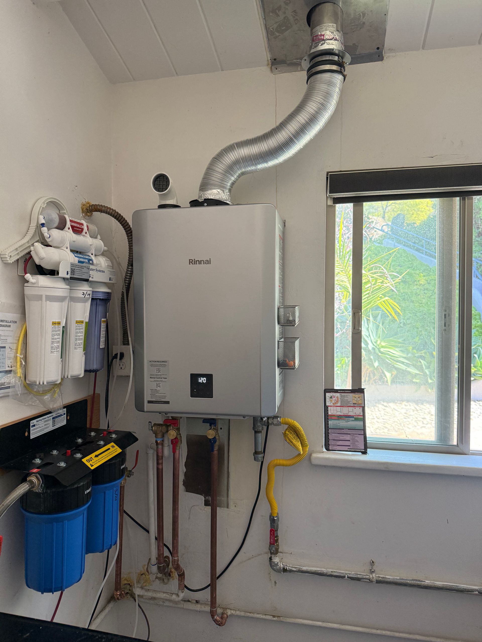 Tankless water heater with metal exhaust vent, installed indoors next to a multi-stage water filtration system.