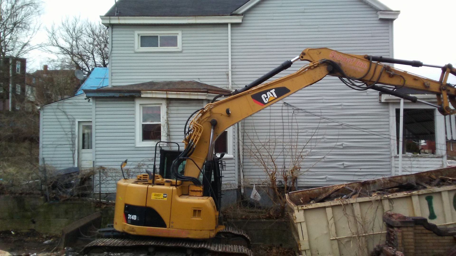 excavator filling a dumpster in front of a house