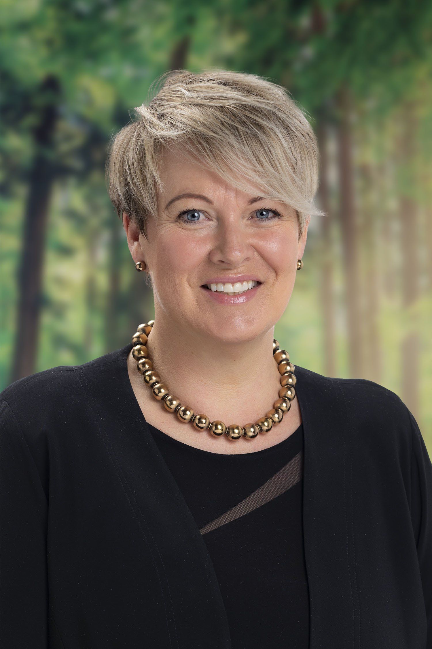 A woman wearing a necklace and earrings is smiling for the camera.