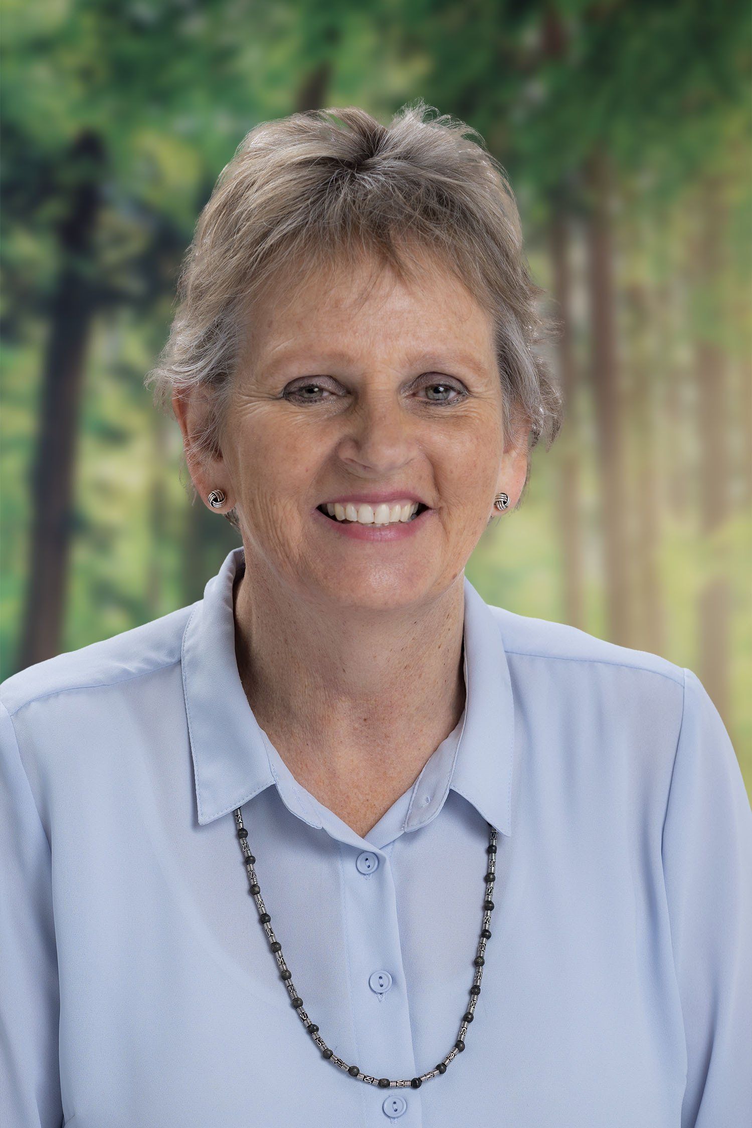 A woman in a blue shirt and necklace is smiling for the camera.