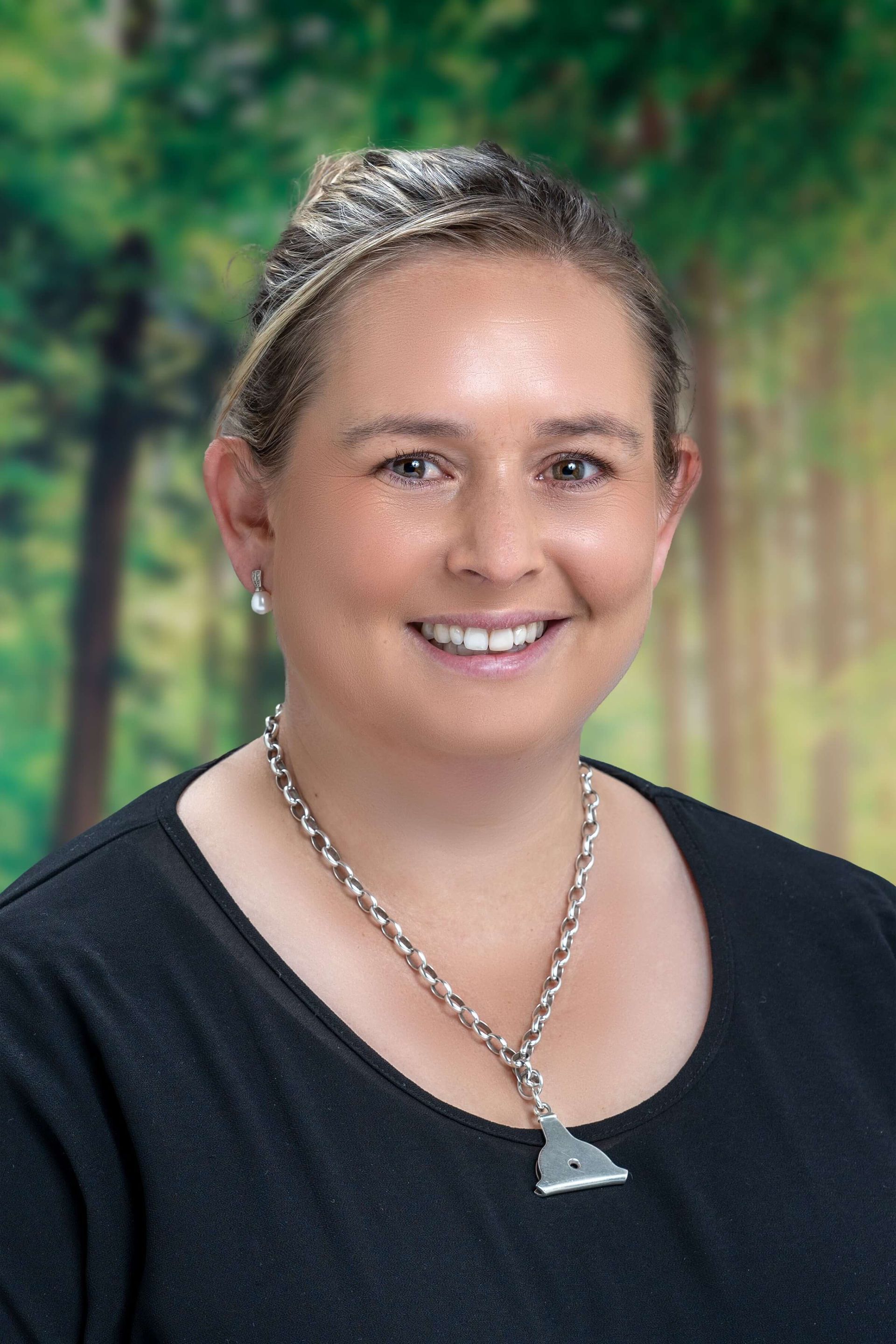 A woman wearing a necklace and earrings is smiling for the camera.