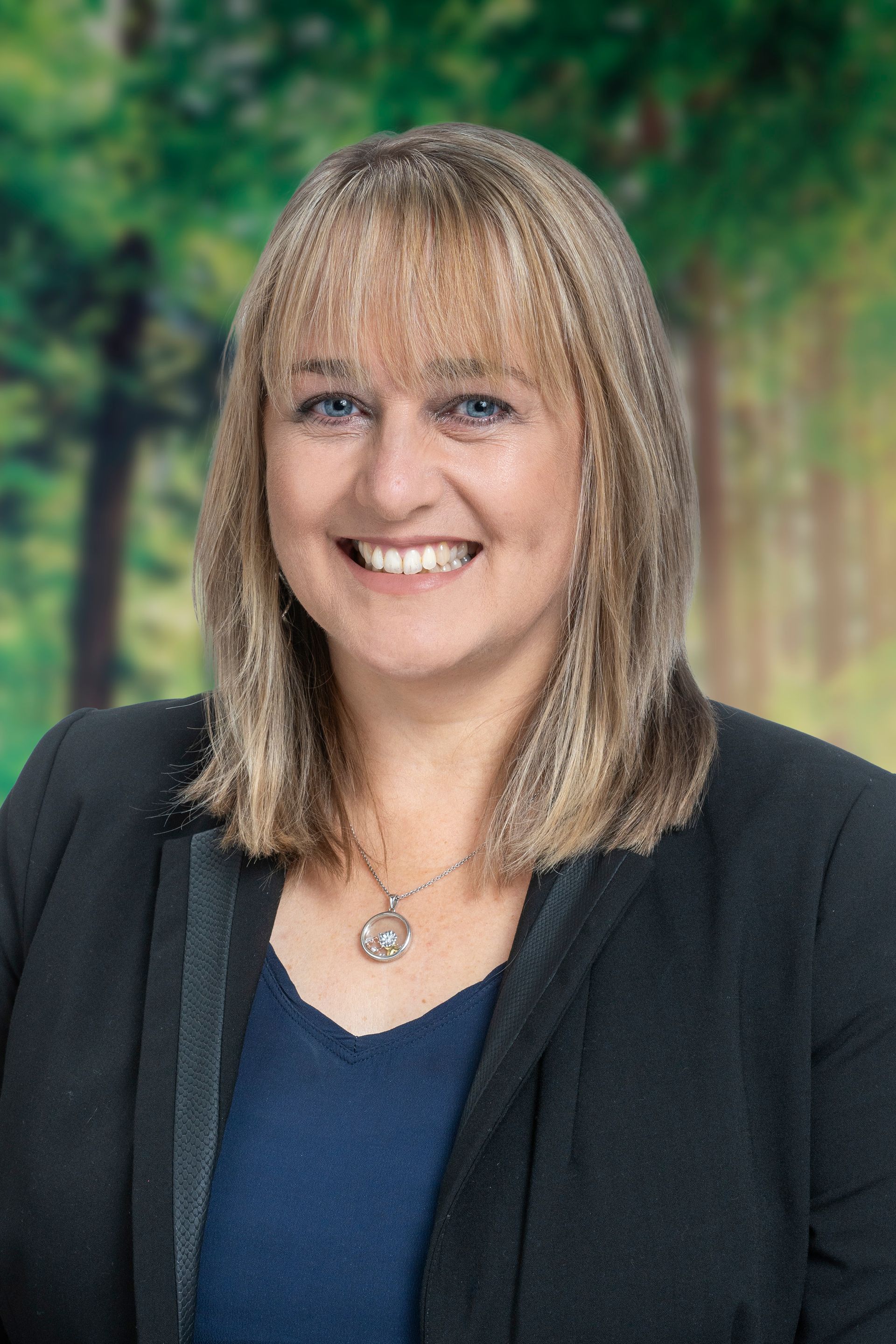 A woman in a black jacket and blue shirt is smiling for the camera.