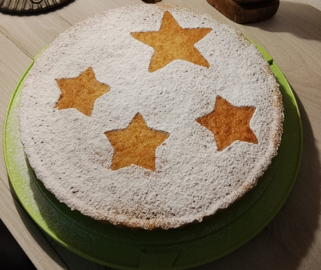 Torta in polvere con quattro stelle arancioni su un piedistallo verde, accanto a piccole statuine di legno su un tavolo