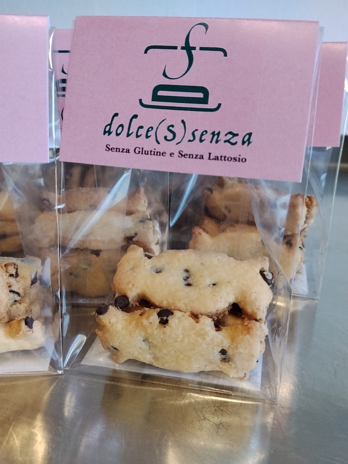 Sacchetto trasparente di biscotti con gocce di cioccolato e un’etichetta rosa con la scritta “dolce(s)enza”.