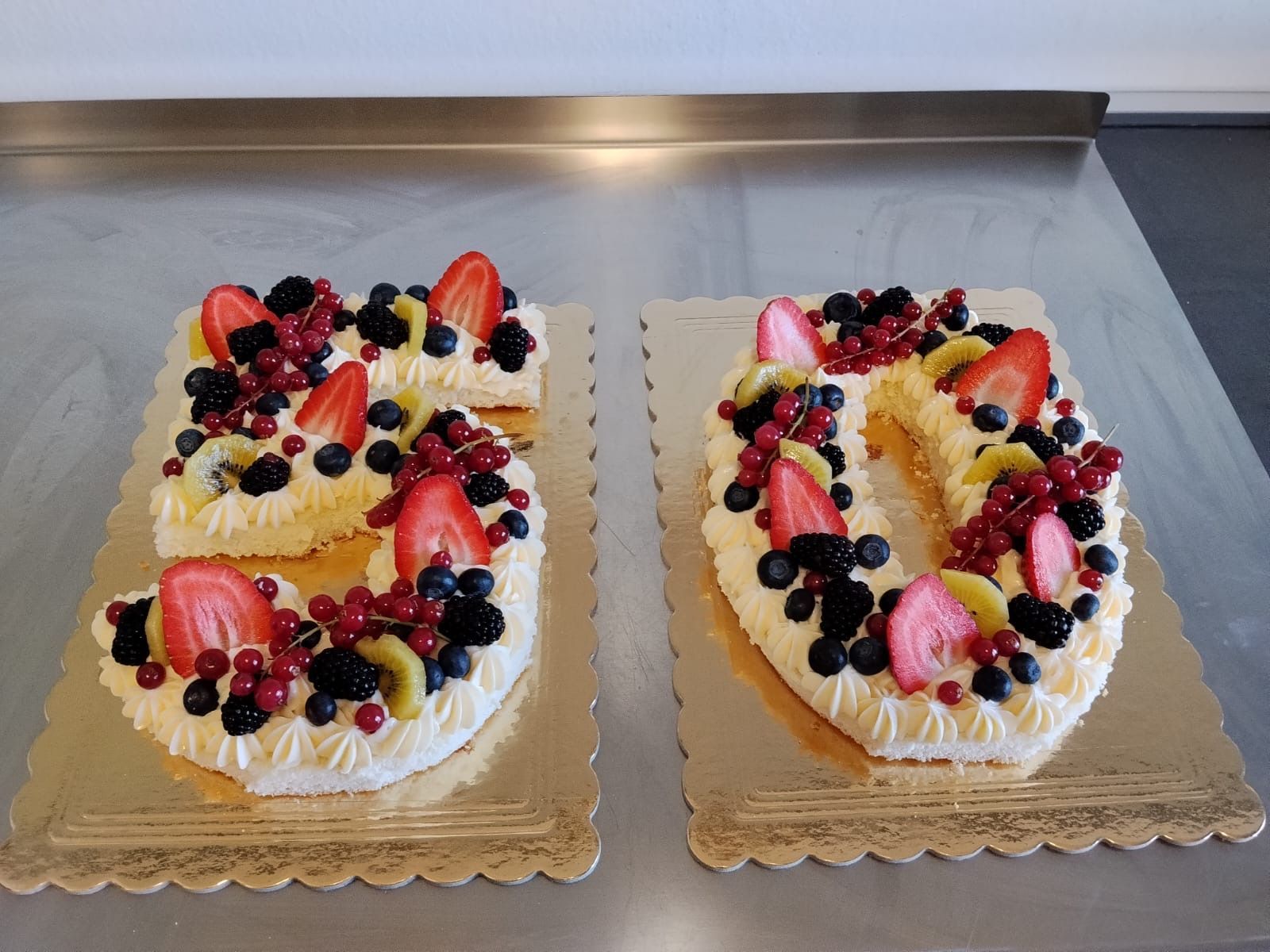 Due torte glassate con frutta, su vassoi dorati, in una vetrina da cucina