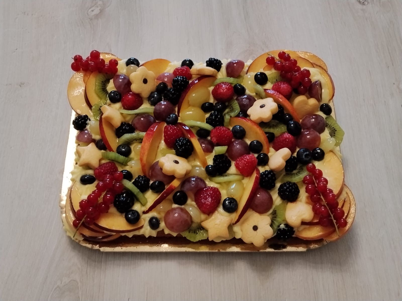 Pasticcino con frutta e glassa lucida, frutti di bosco misti, fettine di mela e uva su una base quadrata