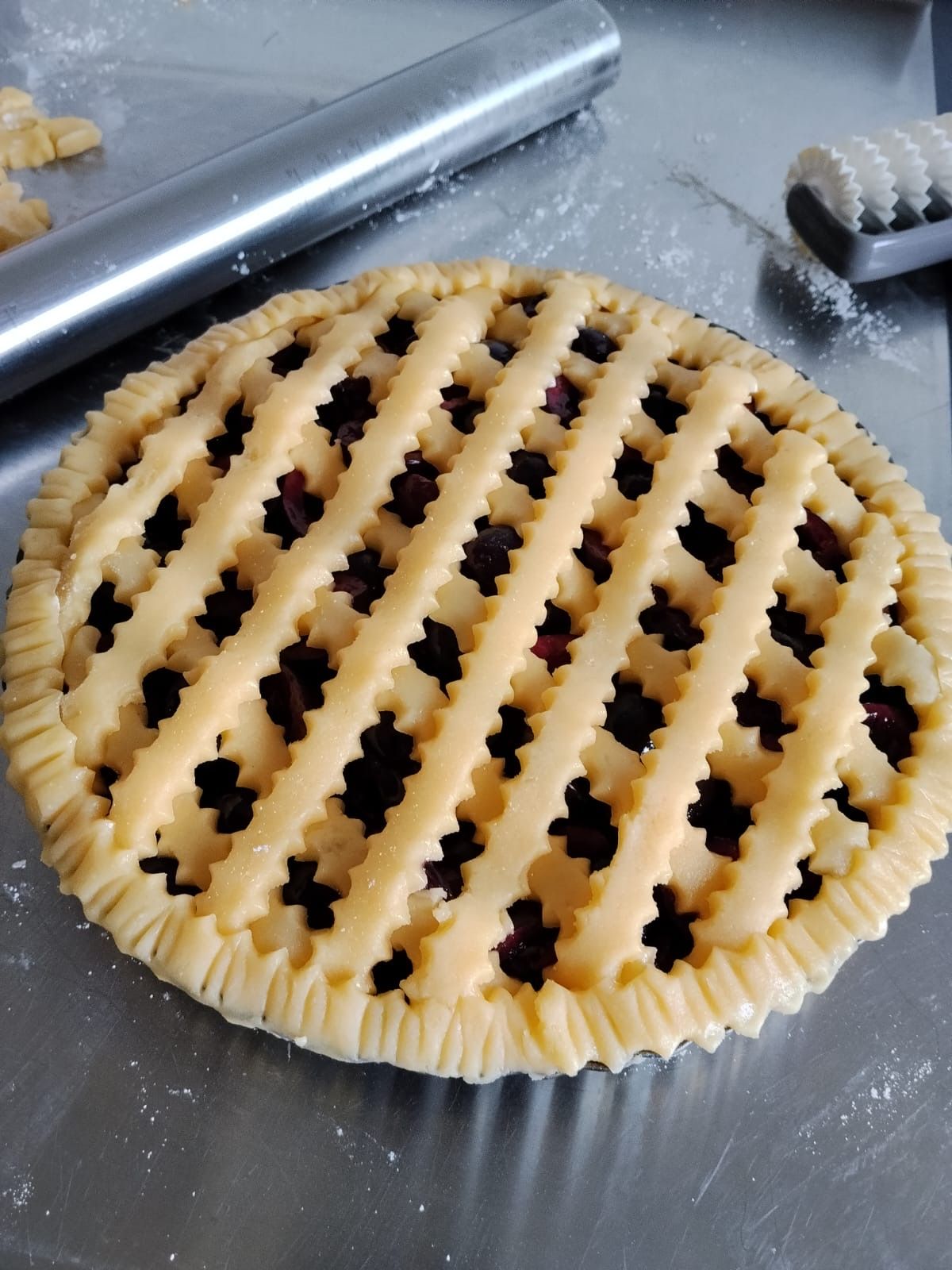 Crostata ai frutti di bosco cruda con griglia in una teglia di alluminio su un piano di lavoro in metallo
