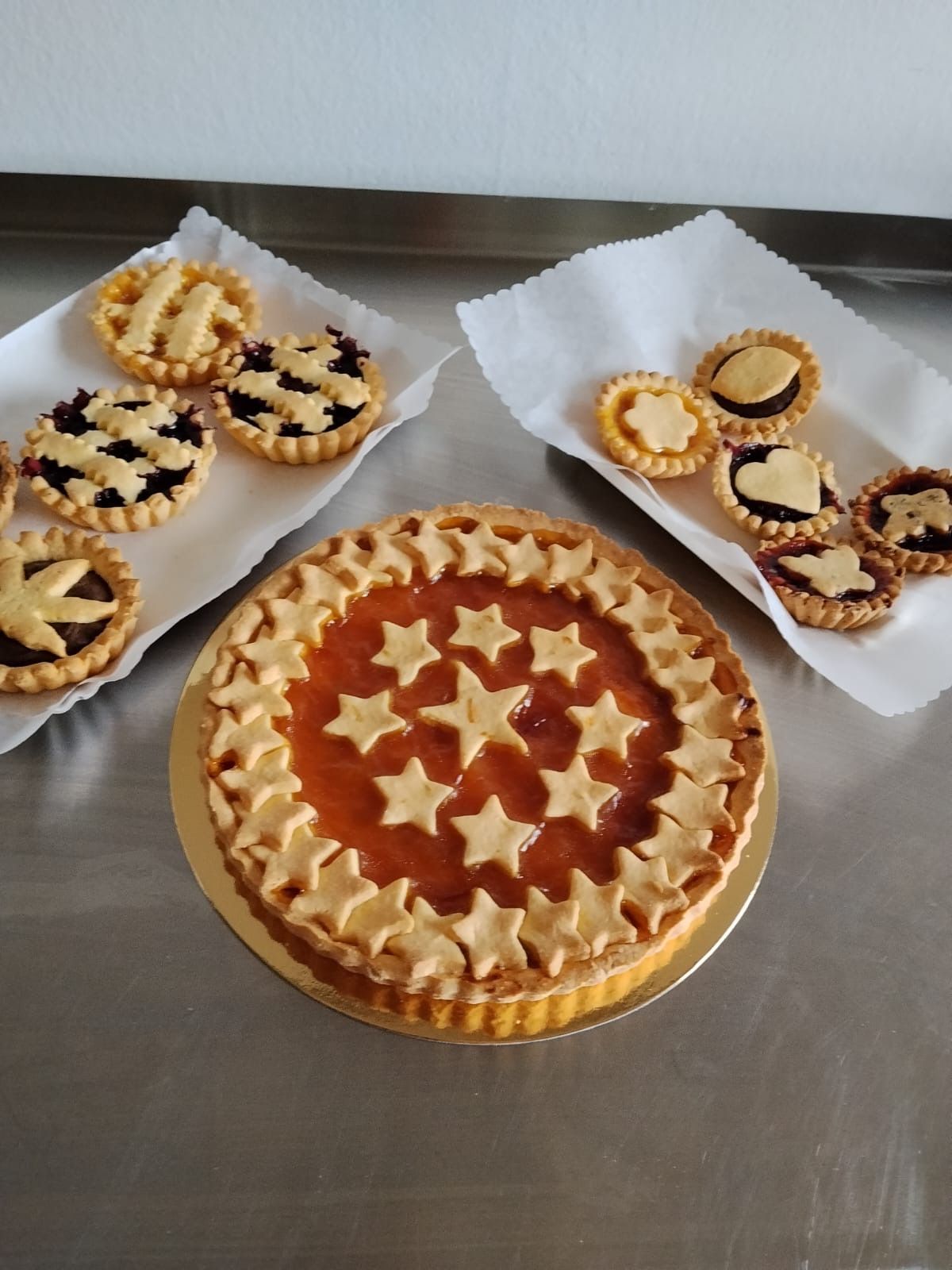 Crostatine assortite su un tavolo di metallo, tra cui una crostata grande decorata con una stella e crostatine più piccole sui tovaglioli.