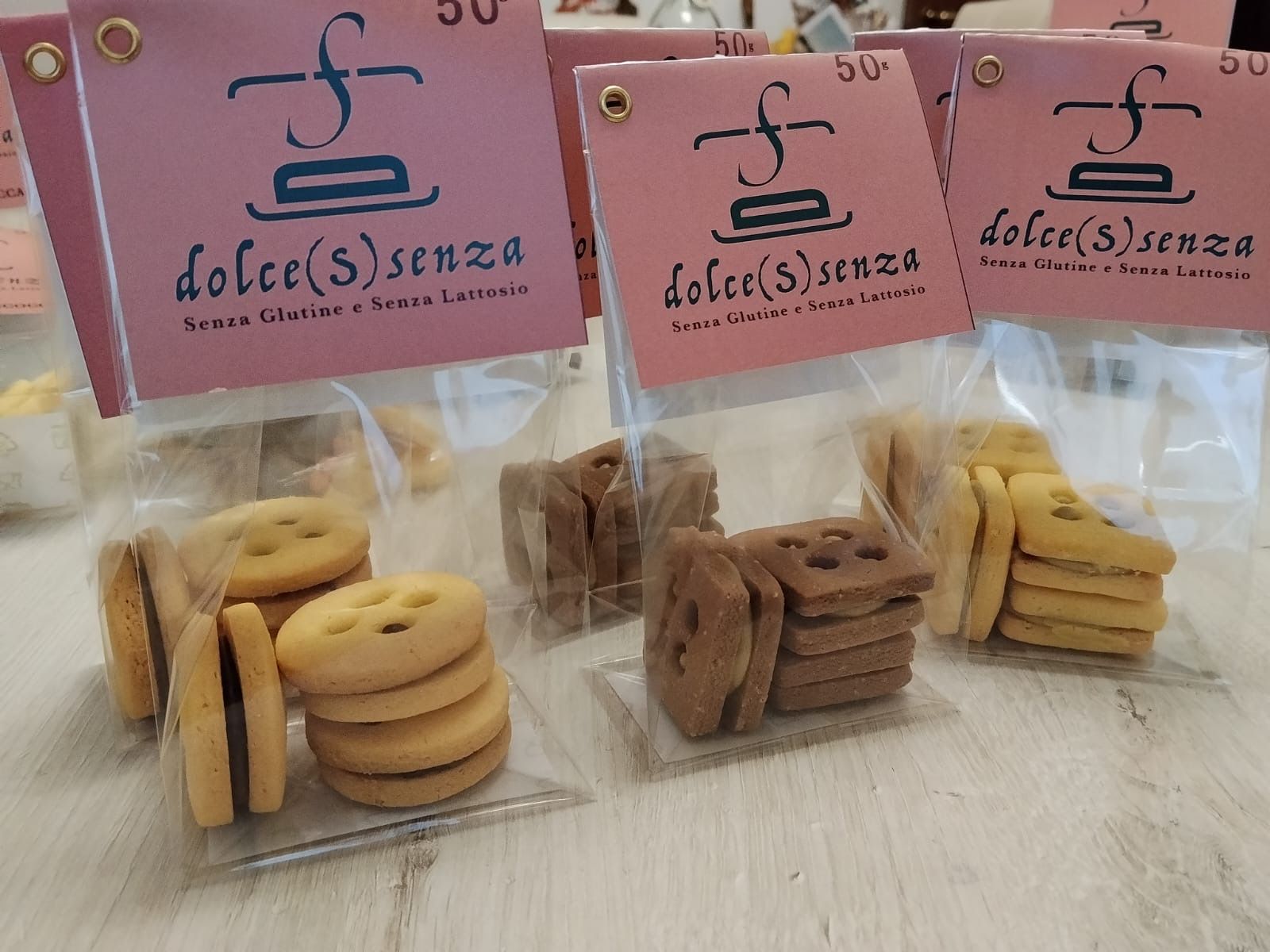 Tre barattoli trasparenti pieni di piccoli biscotti, con etichette rosa da pasticceria, su un tavolo