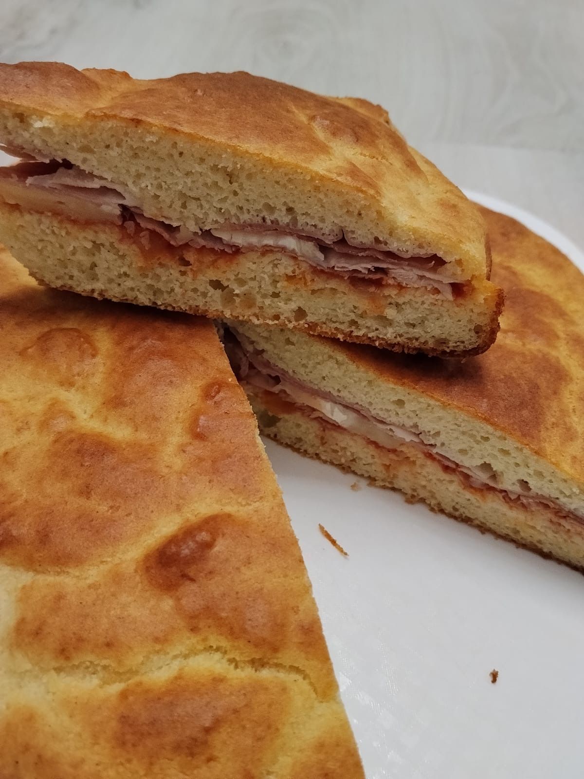 Focaccia ripiena a fette su un piatto bianco, con la crosta dorata e il ripieno rossastro visibile all’interno
