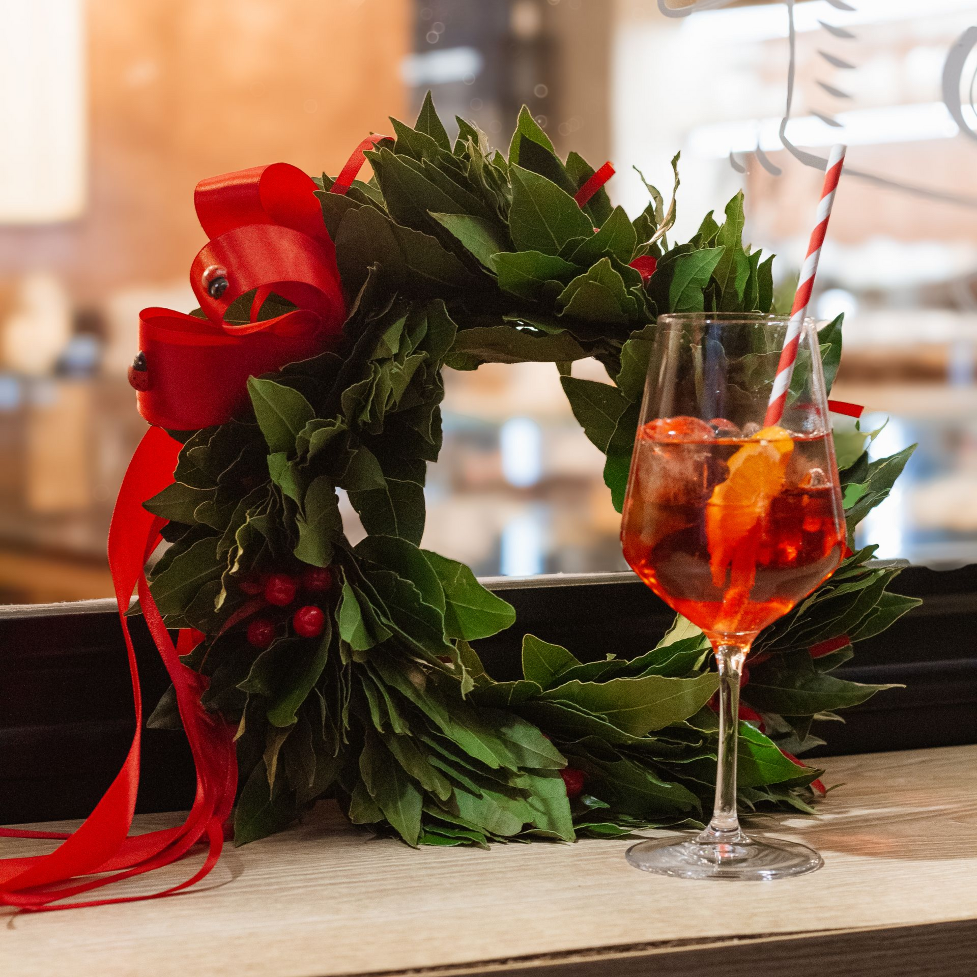 Cocktail festivo in un bicchiere, fetta d'arancia, cannuccia, accanto a una ghirlanda verde con fiocco rosso.