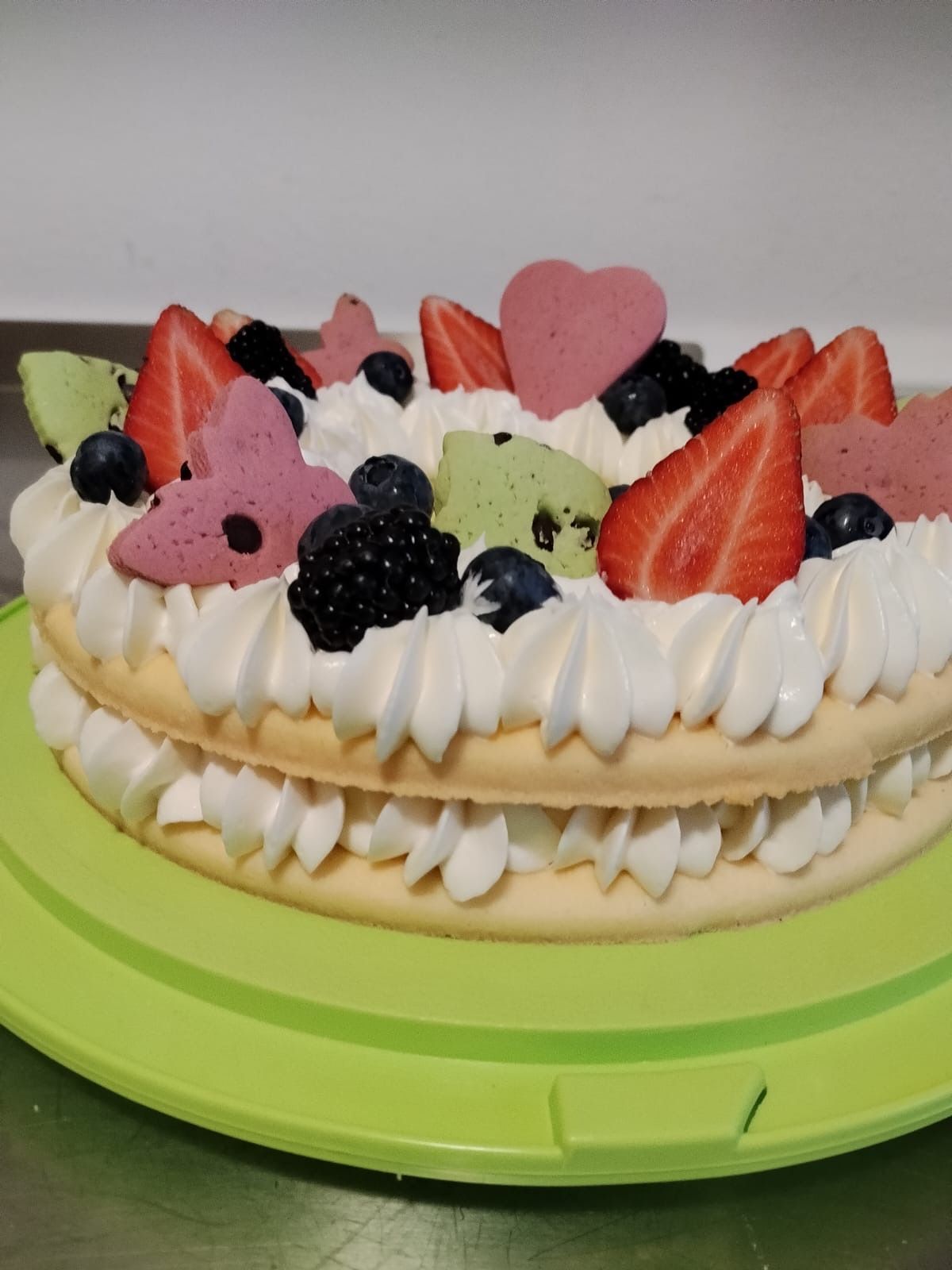 Torta bianca con panna montata, fragole, frutti di bosco e decorazioni a forma di cuore rosa su un’alzatina verde