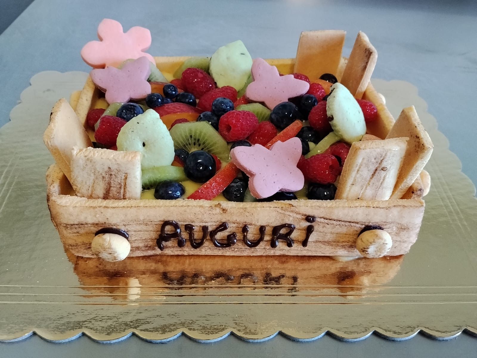 Crostata alla frutta in un cestino di vimini, ricoperta di frutti di bosco e kiwi, con la scritta “AVOURI” sul davanti.