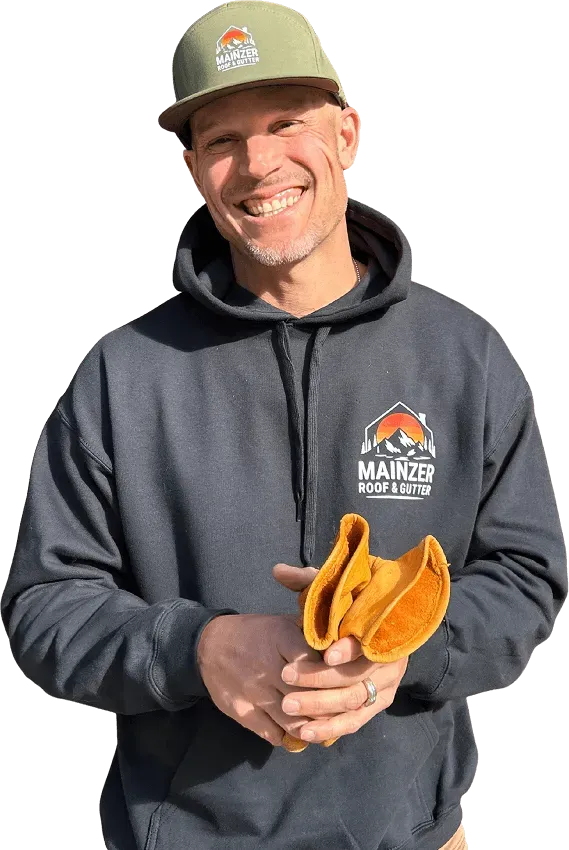 Smiling worker in green cap and dark hoodie holding two orange gloves on a white background