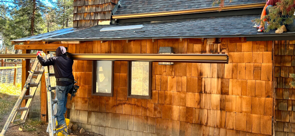 Person on a ladder working on the roof of a wooden cabin with cedar shingles