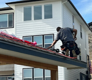 Worker installing roofing on a two-story house with white siding