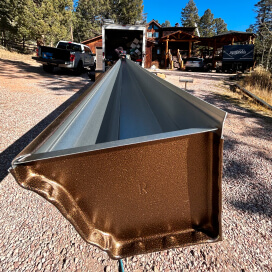 Long metal gutter section on a gravel driveway, with a truck and garage in the background.