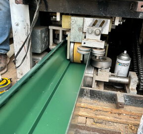 Industrial machine with green metal channel and roller assembly in a workshop.