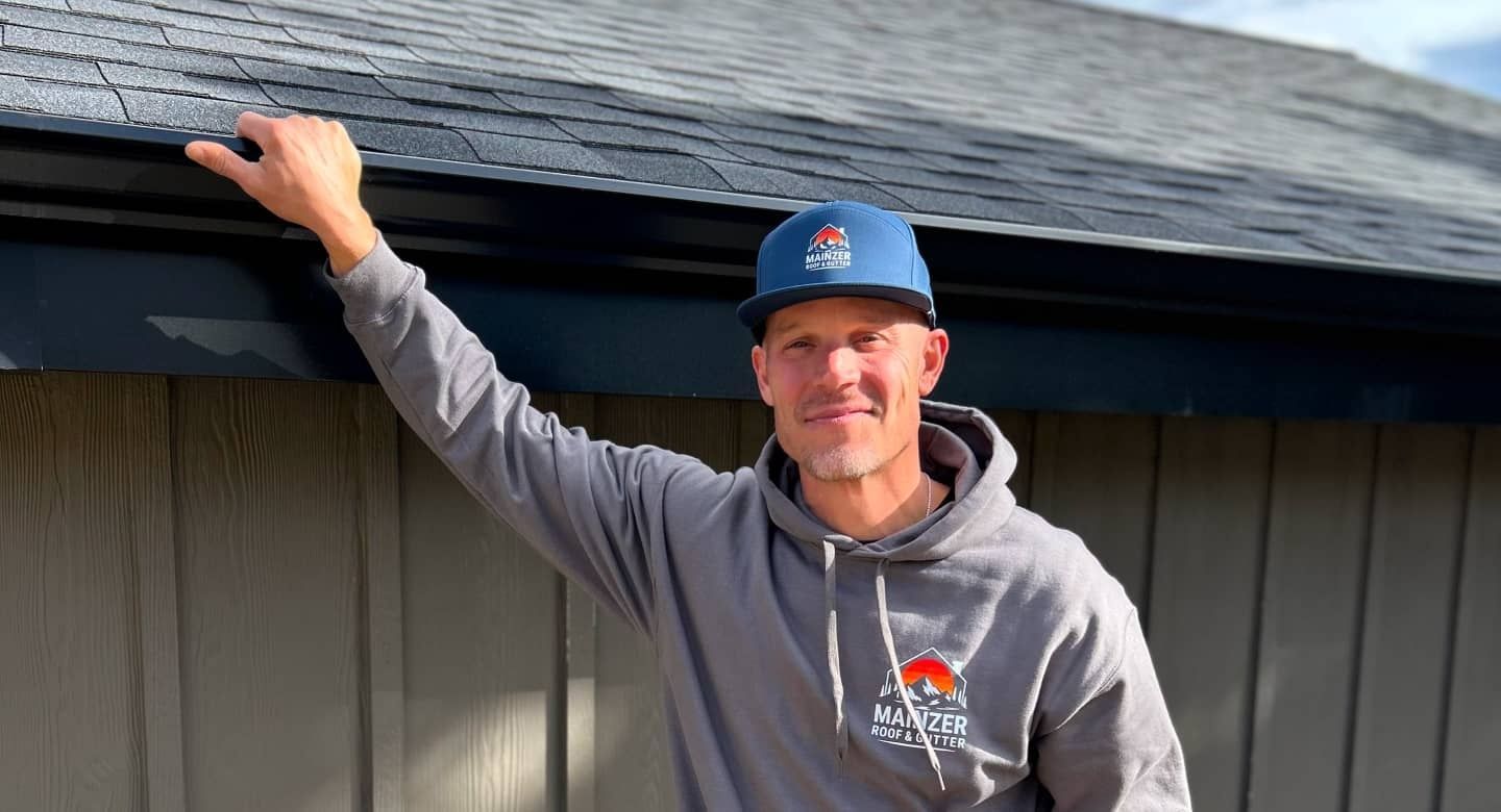 Man in gray hoodie and blue cap leaning on a roof edge outside a building
