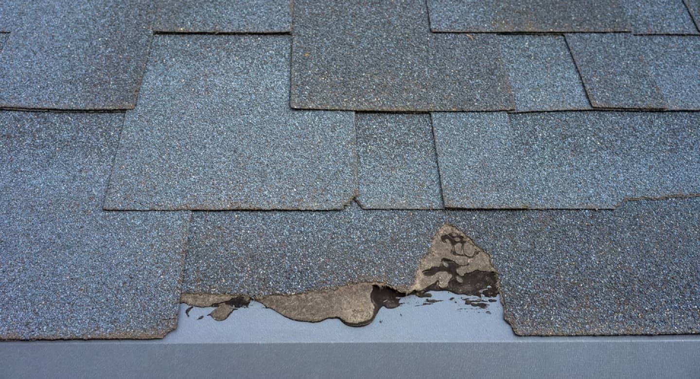 Damaged gray roof shingles with a hole exposing the underlayment below