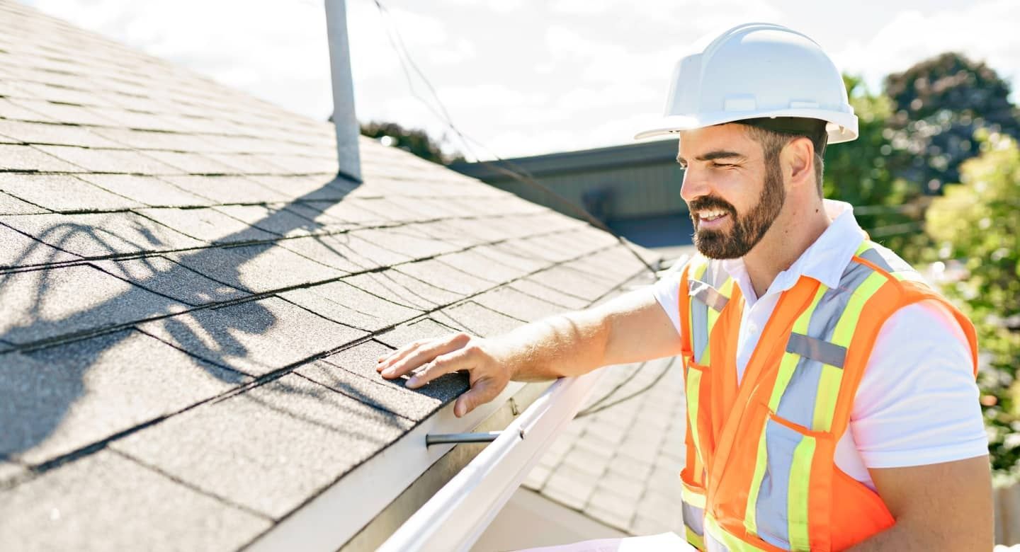 Worker in hard hat and safety vest inspecting solar panels on a rooftop under bright sunlight